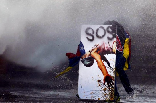 Un manifestante contra el gobierno se refugia de los cañones de agua de la policía detrás de un escudo improvisado en Caracas.